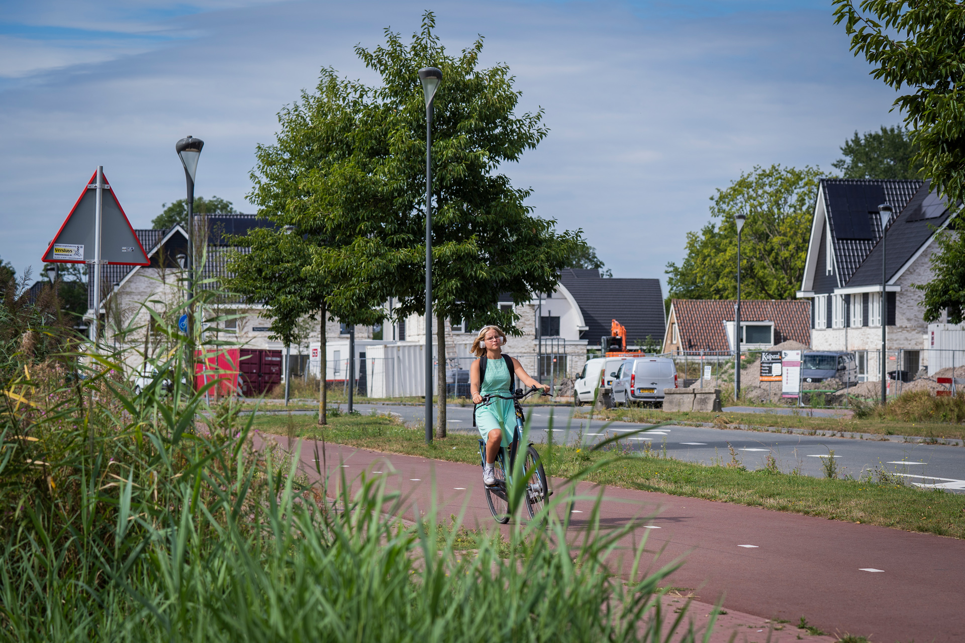 Fietsster fietst op een vrijliggend geasfalteerd roodkleurig fietspad. Op de achtergrond zijn woningen te zien.