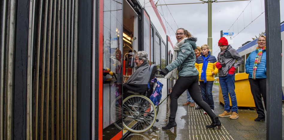 vrouw duwt persoon in rolstoel in tram