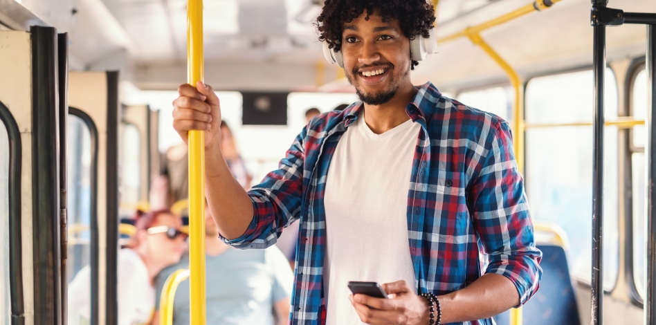 Een lachende jongeman die zich vasthoudt aan een van de gele palen in de bus.