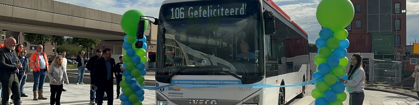 Een bus met de tekst Gefeliciteerd op het display rijdt door een lint om zo het vernieuwde busstation Spijkenisse Centrum te openen. Mensen staan toe te kijken.