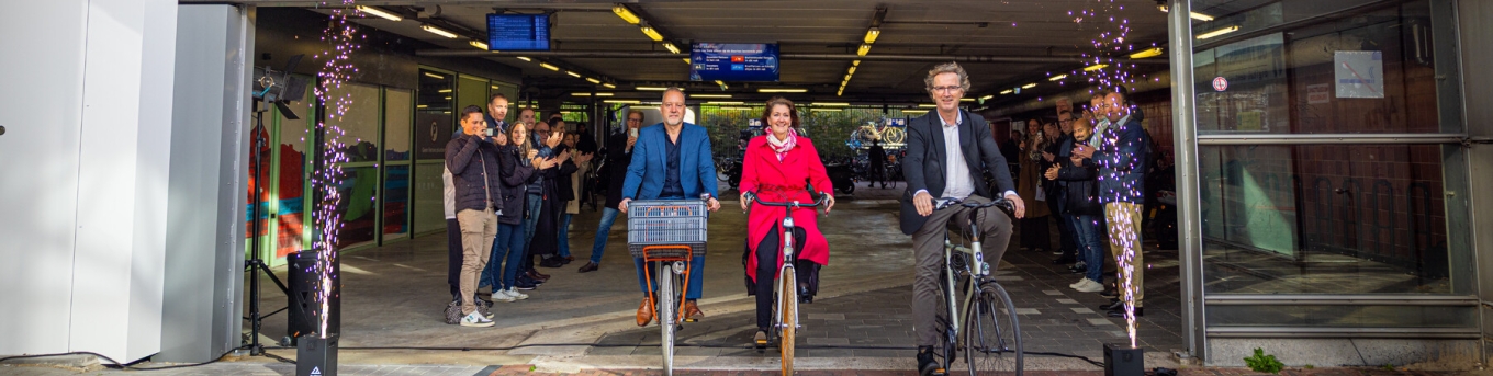 Jan-Willem Immerzeel (MRDH), Helga Cuijpers (ProRail) en wethouder Frans Hamerslag (Schiedam) komen fietsend uit de nieuwe fietsenstalling bij Schiedam station
