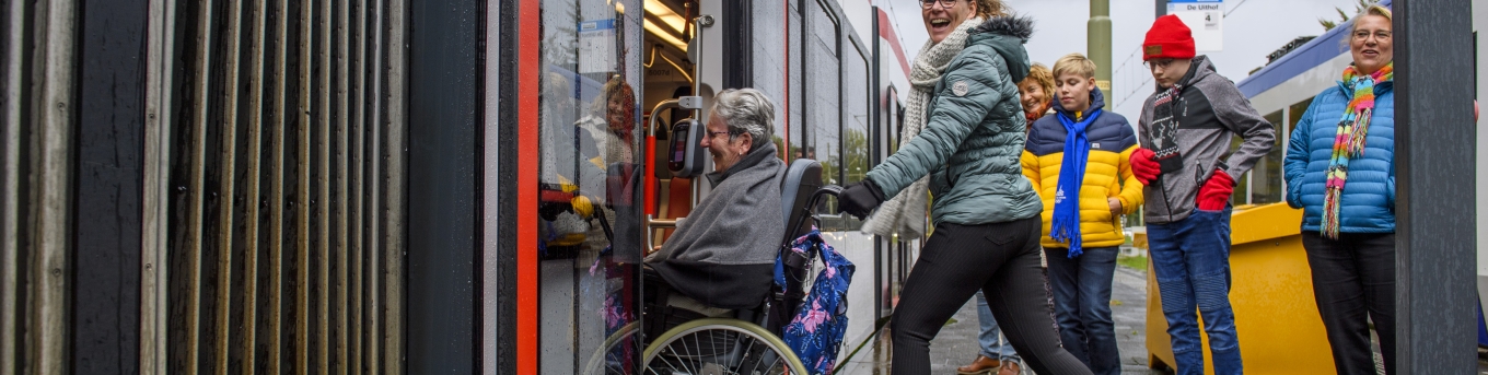 vrouw duwt persoon in rolstoel in tram