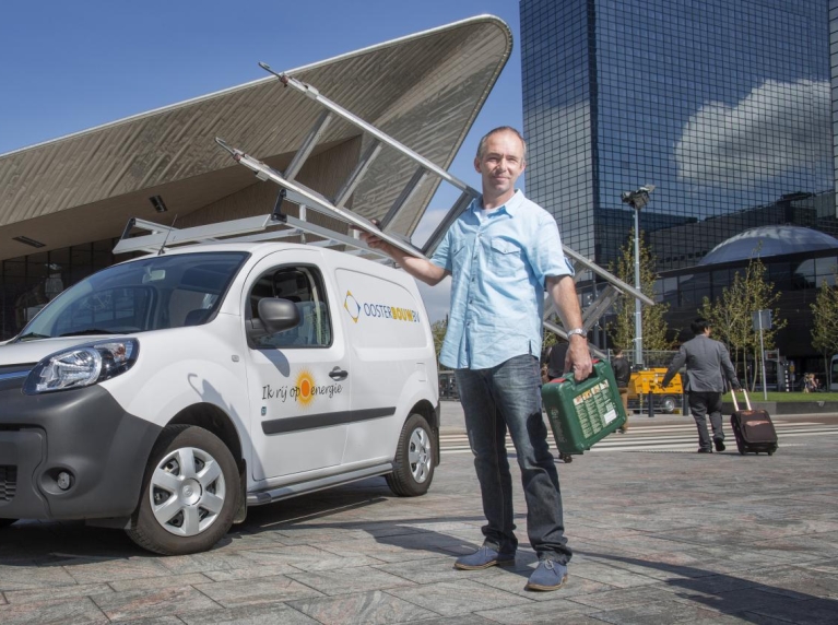 Een loodgieter staat met zijn ladder bij zijn uitstootvrije bestelbus voor het centraal station van Rotterdam