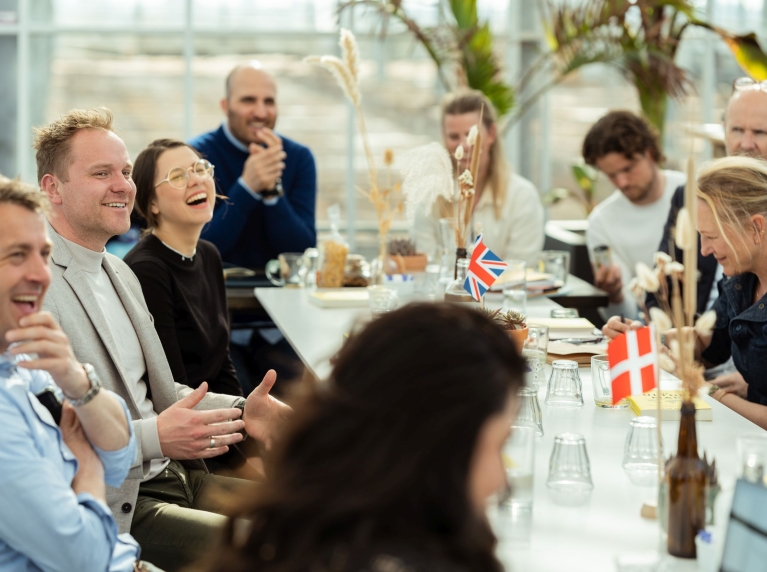 Mensen zitten aan een tafel in gesprek en lachen. Op tafel staan internationale vlaggetjes van landen.