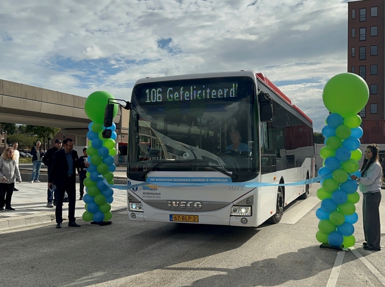 Een bus met de tekst Gefeliciteerd op het display rijdt door een lint om zo het vernieuwde busstation Spijkenisse Centrum te openen. Mensen staan toe te kijken.
