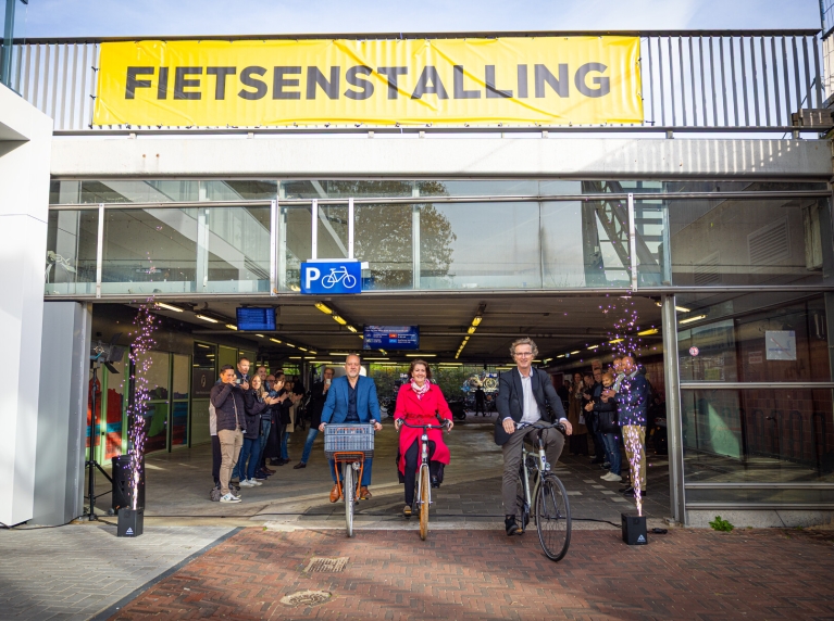 Jan-Willem Immerzeel (MRDH), Helga Cuijpers (ProRail) en wethouder Frans Hamerslag (Schiedam) komen fietsend uit de nieuwe fietsenstalling bij Schiedam station