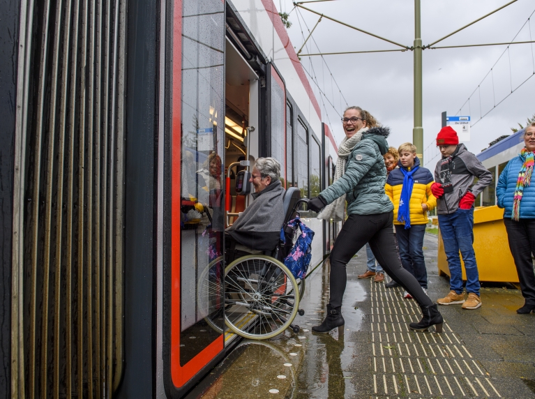 vrouw duwt persoon in rolstoel in tram