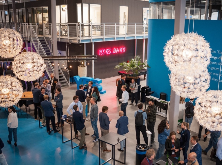Een groep mensen staat in de aula van Yes!Delft 